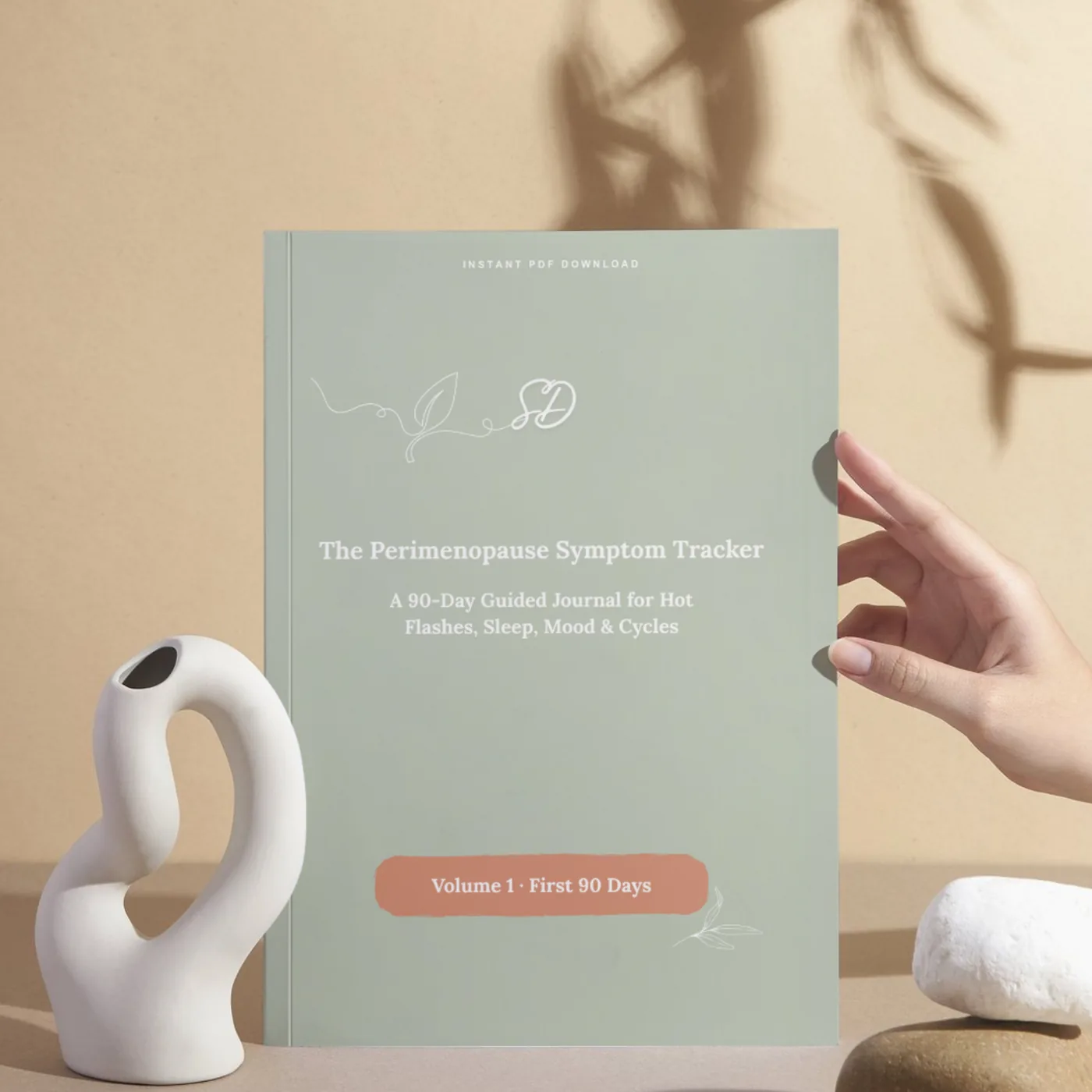 A hand holding the sage-green Perimenopause Symptom Tracker against a warm beige background